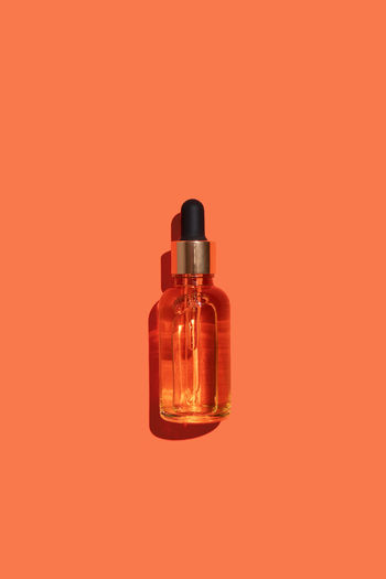 Glass dropper bottle on orange background. hyaluronic acid oil, serum with collagen and peptides 