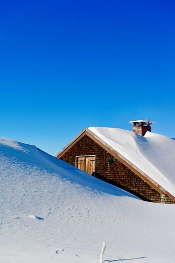 Snow covered house at mountain against clear blue sky