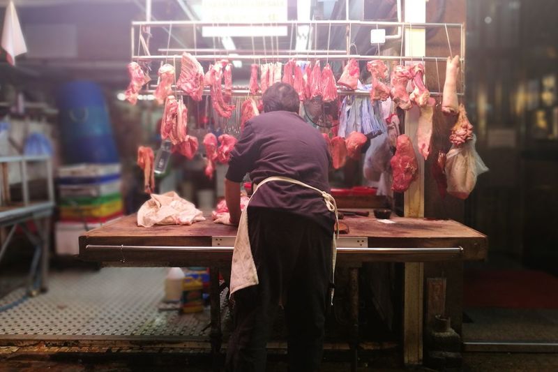 Rear view of butcher with fresh meat in shop