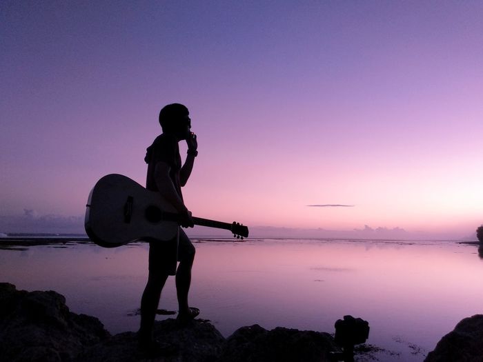 Silhouette man standing on rock against sky during sunset