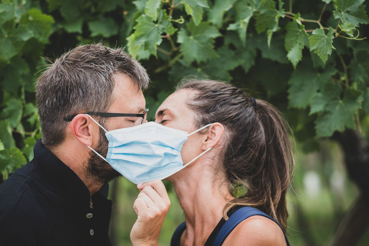 Couple of lovers kissing behind protective mask - normal lifestyle concept with couple in love kiss 