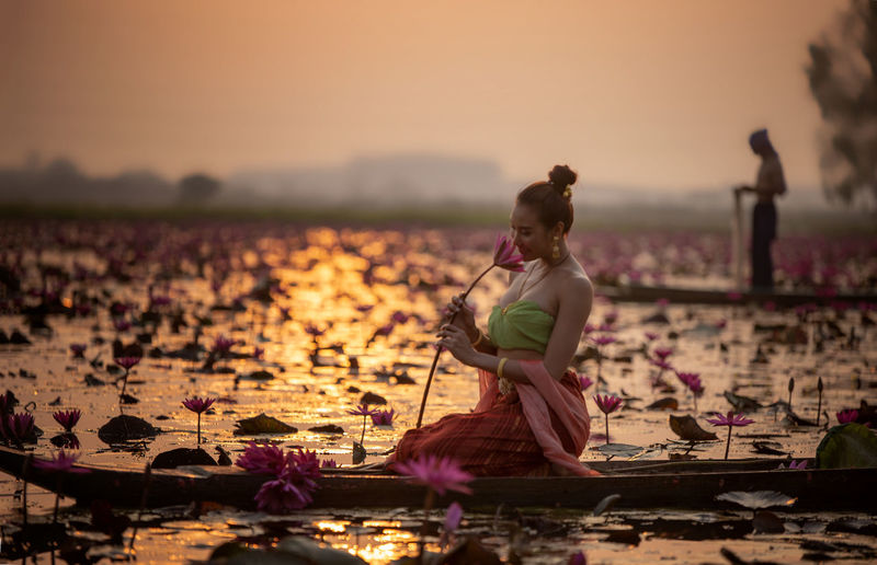Woman holding lotus while sitting on boat in lake
