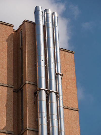Three big vertical steel pipes attached to the exterior wall of a building.