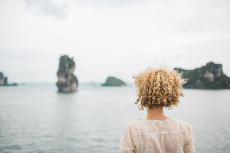 Rear view of woman with curly hair looking at sea against sky