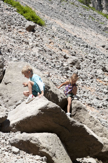 Cute sibling sitting on rock outdoors
