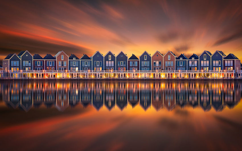 Reflection of building on sea against cloudy sky during sunset