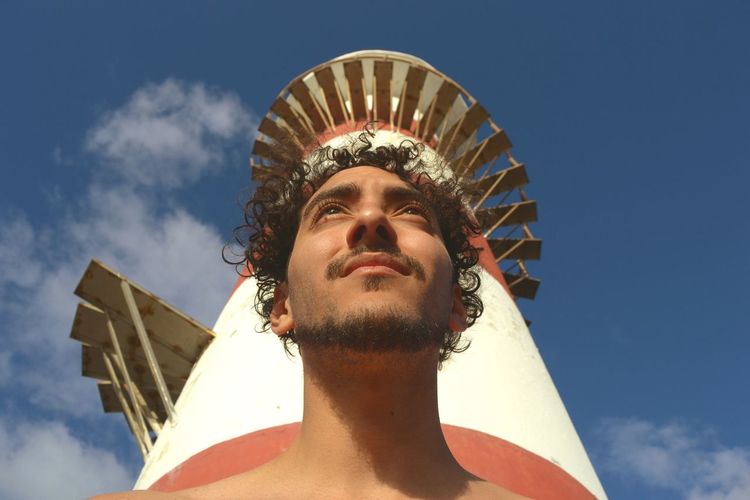Low angle view of young man standing by built structure against sky