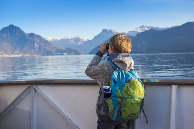 Rear view of boy standing by sea against mountains