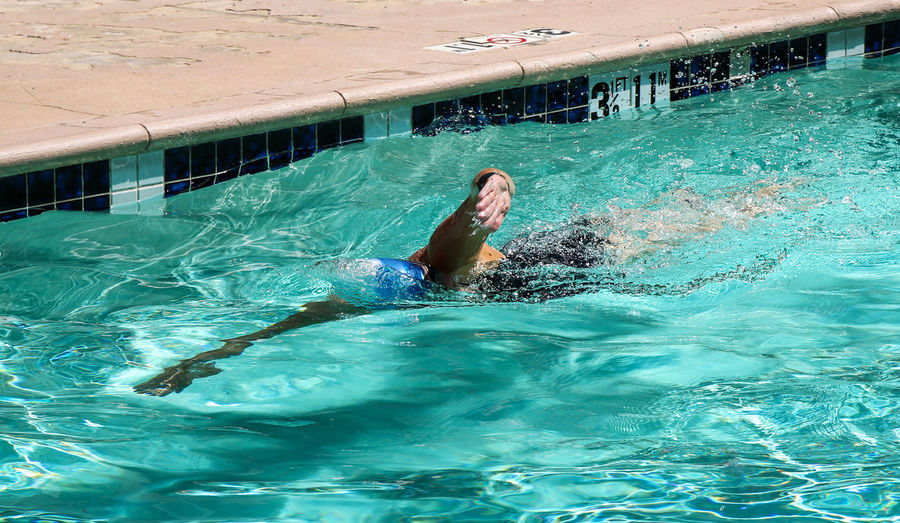 One female swimmer swimming laps in an outdoor pool at a hotel wearing a swim cap.