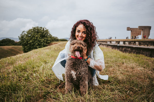 Portriat of woman with dog crouching on grass against sky