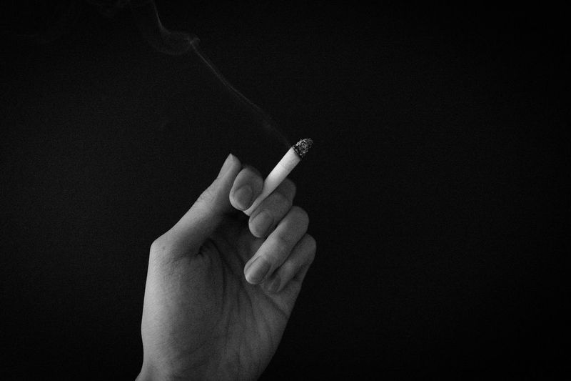 Cropped image of hand holding cigarette against black background