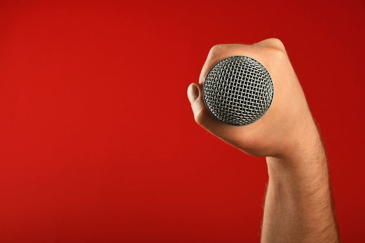 Cropped image of musician holding microphone against red background
