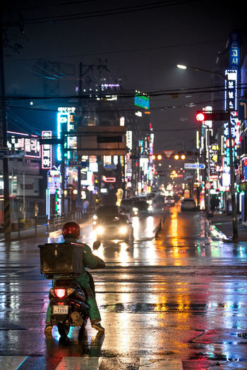 Rear view of man sitting on wet street at night