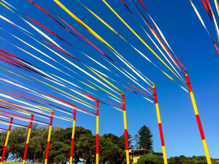 Low angle view of colorful ribbon decoration on poles against clear sky