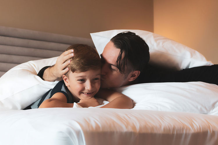 Caring father kissing his small son while relaxing in bedroom together.