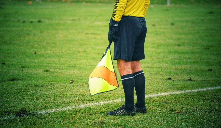 Low section of referee holding flag while standing on sports field