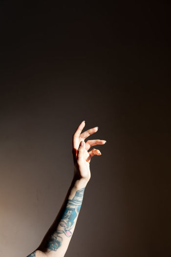Low angle view of tattooed woman's hand against dark background