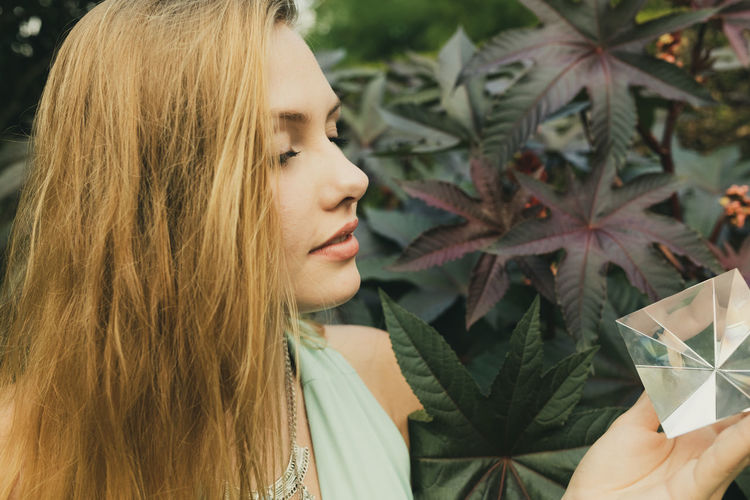 Young woman looking at prism while standing against plant
