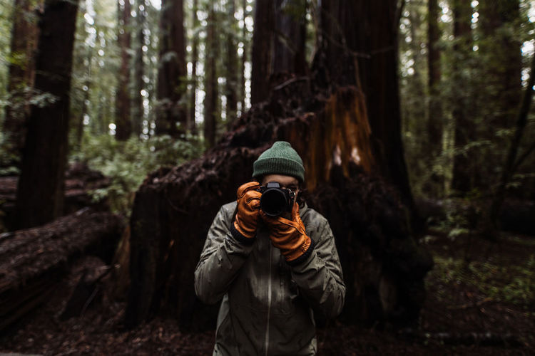 Unrecognizable male traveler taking photo on professional photo camera while standing in woods in fall