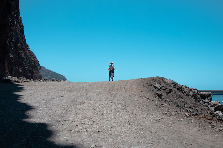 Man standing on shore against clear blue sky