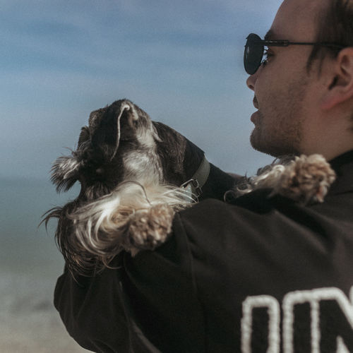A young guy hugs his miniature schnauzer dog against the backdrop of the sea