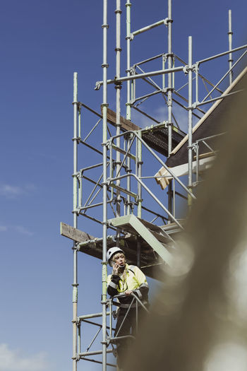 Female builder talking on mobile phone while standing at scaffolding
