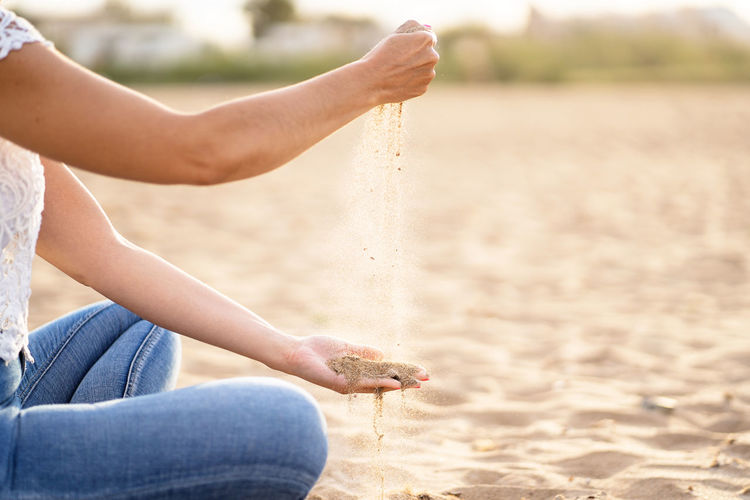 Unrecognizable woman playing with the sand in the beach. horizontal view of summer relax background.