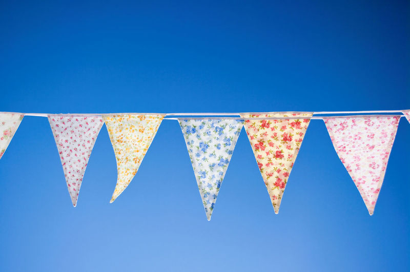 Low angle view of bunting flags hanging against clear blue sky