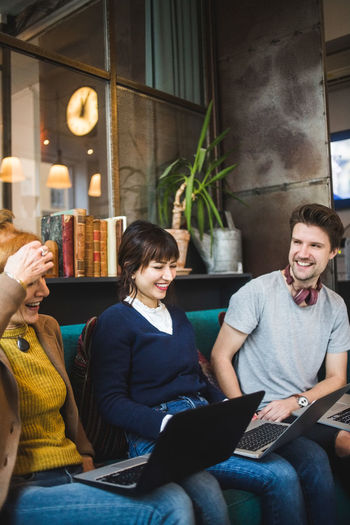 Smiling male and female colleagues looking at female manager sitting with laptop on sofa at creative office