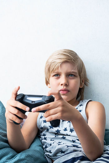 Boy holding joystick gaming controller in hands, playing video game at home.