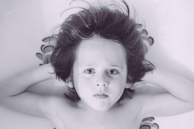 High angle portrait of shirtless boy lying on bed
