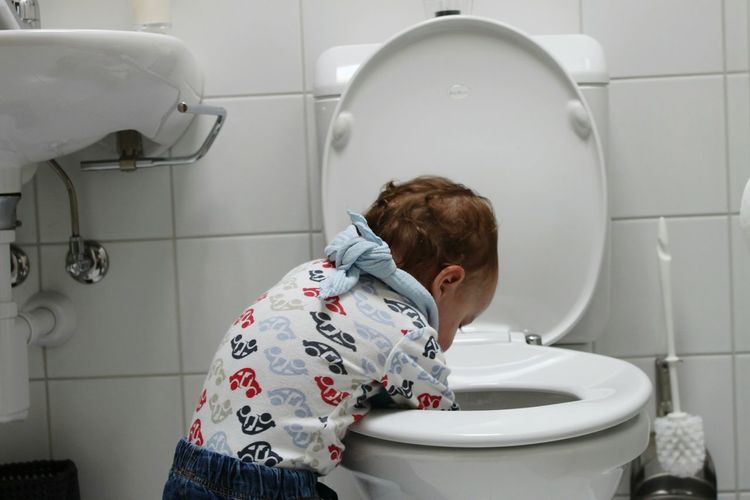 Rear view of boy with hands in toilet