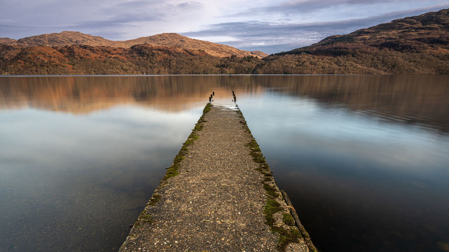 An old jetty on the shore of loch lomond, scotland. looking over to inversnaid and the mountains.
