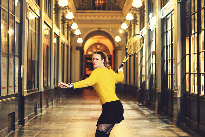 Portrait of woman with badminton racket standing in corridor of building