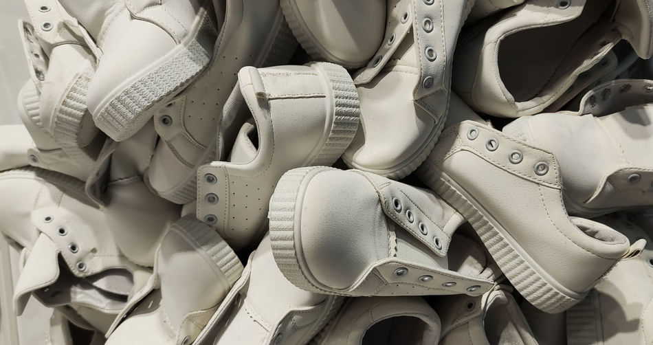 A large number of identical sports shoes. lots of white sneakers shoes. a pile of shoes without