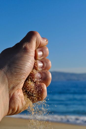 Close-up of hand holding sand against sea and clear blue sky