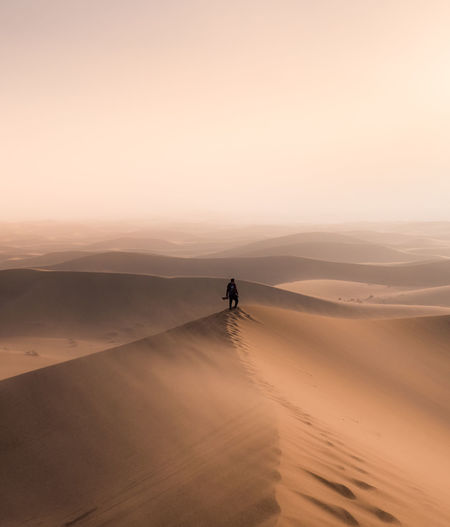 Man standing at desert against sky during sunset