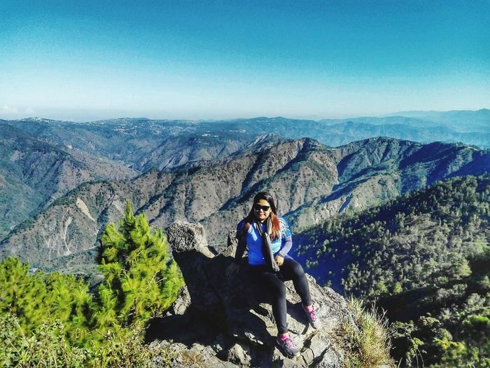 Portrait of woman sitting on cliff with mountains in background