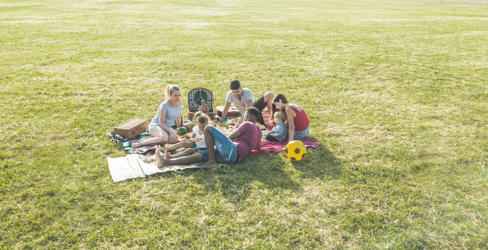 High angle view of family friends sitting on grassy field during picnic