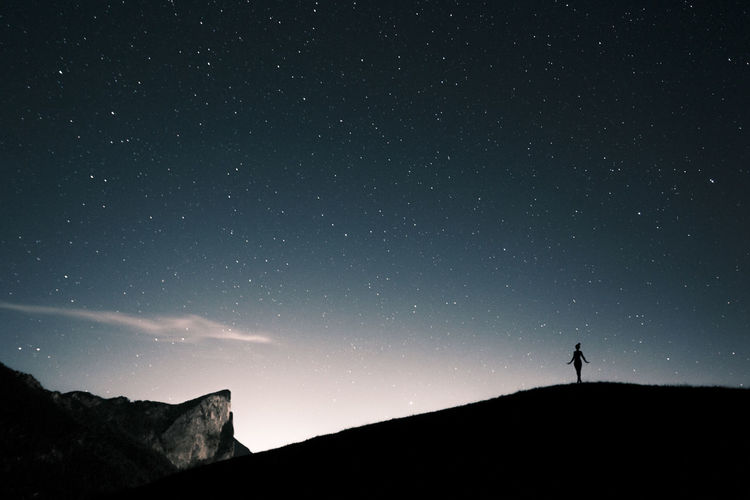Silhouette person standing on mountain against sky at night