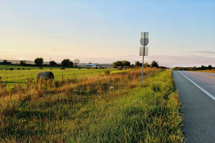 Agricultural field by empty road against sky during sunset