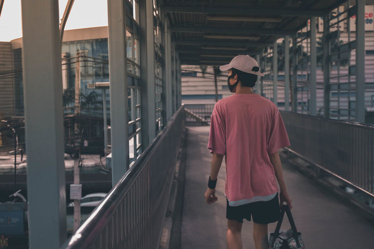 Rear view of man walking on footbridge in city