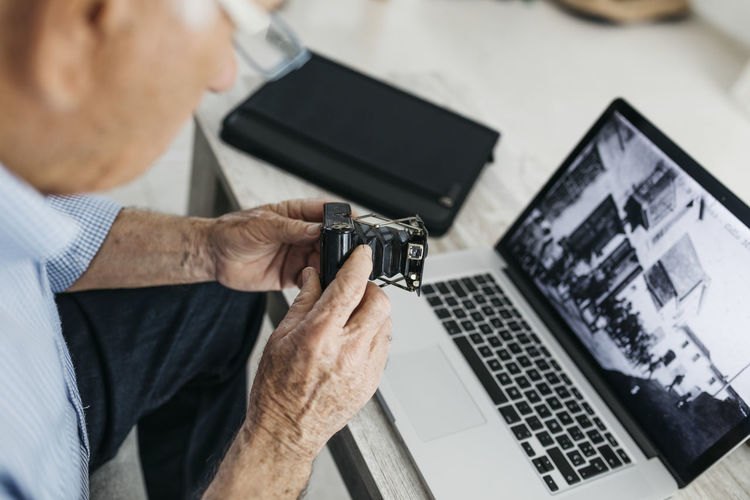 Senior man using laptop and holding his old photo camera, screen with old photo