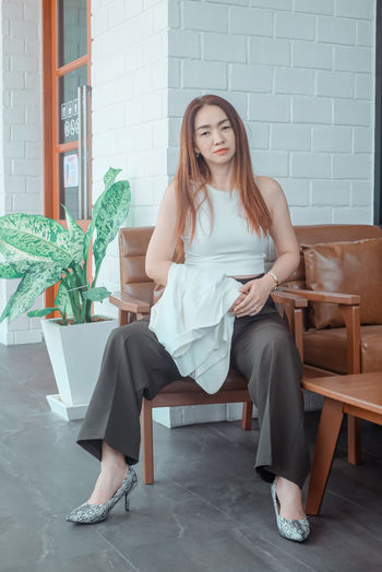 Portrait of woman sitting on chair against wall