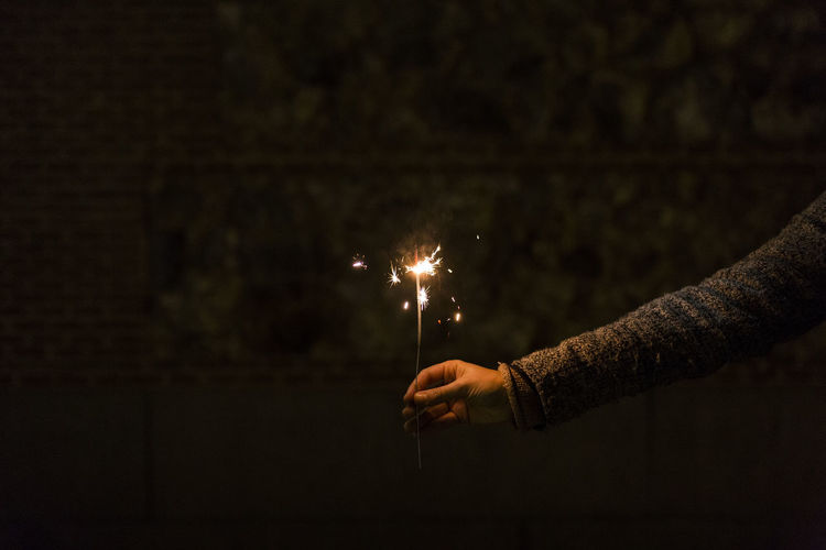 Cropped hand of person holding sparkler at night