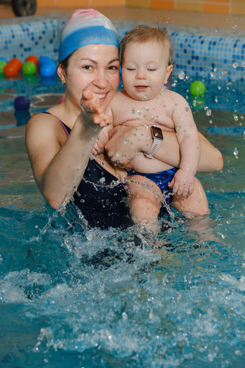 Early swimming coach training to swim baby boy in indoor pool. playing activity for infant with
