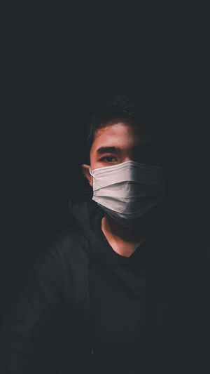 Close-up portrait of young man wearing mask against black background