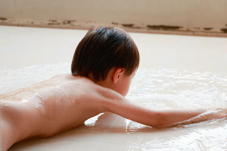 Close-up of shirtless boy lying on wet floor