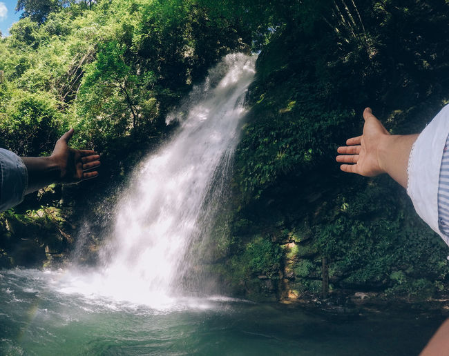 Cropped hand of person gesturing against waterfall