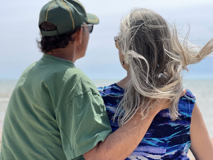 Active senior couple on beach looking out on water with his hand on her shoulder.  close-up.  